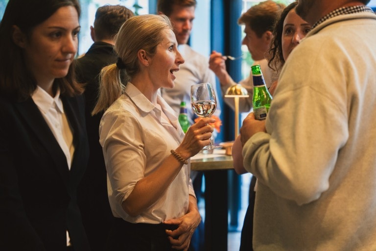 Socialising at a lively gathering, people engaging in animated conversations with drinks, warm lighting, and a welcoming atmosphere.