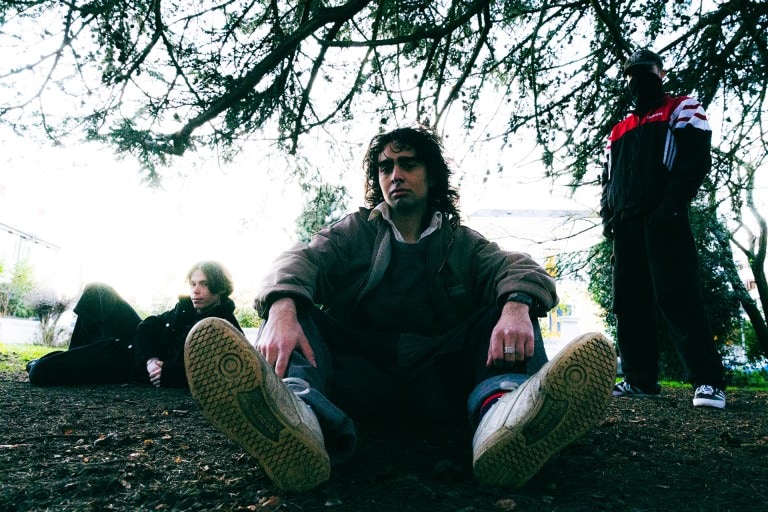 Young people sitting outdoors beneath tree branches, conveying a rebellious and contemplative mood.