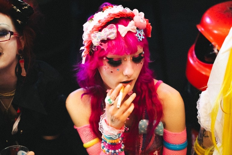 Vibrant alternative fashion portrait of a woman with vivid pink hair, goth makeup, and eclectic accessories at a themed event.