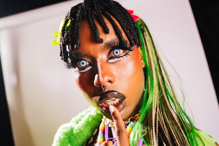 Vibrant portrait of a woman with bold makeup, colourful accessories, and distinctive hairstyle, showcasing creative fashion photography.