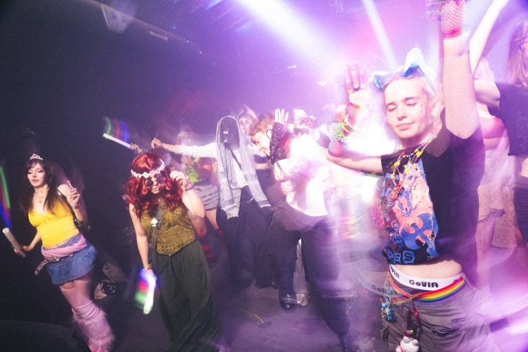 Vibrant LGBTQ+ themed dance party with colourful outfits and energetic atmosphere at a nightclub.
