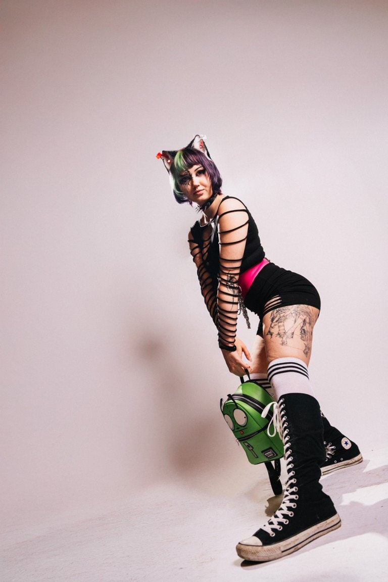 Vibrant alternative fashion portrait of a woman dressed in edgy, gothic-inspired outfit with colourful hair and tattoo artwork.