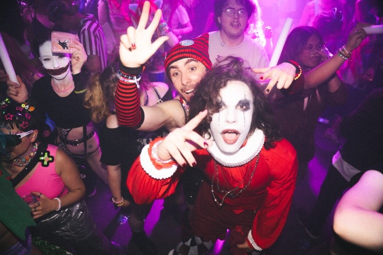 Vibrant Halloween themed party with costumed guests, spooky makeup, and colourful lighting in a lively dance setting.