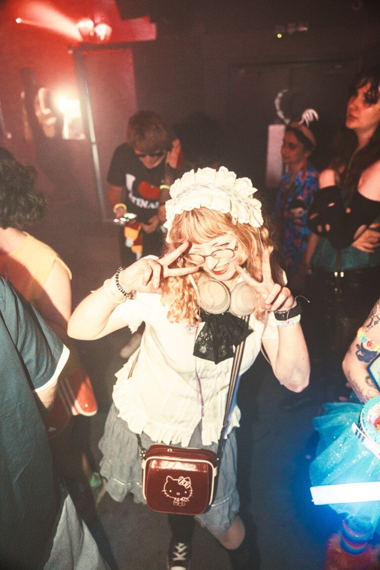 Vibrant dance party scene with young woman wearing floral headband, making peace signs at nightclub, capturing energetic nightlife photography.