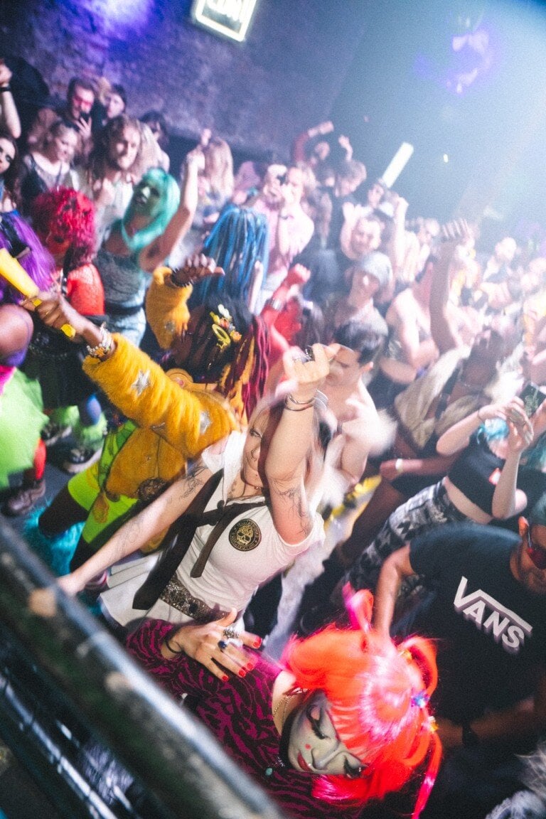Vibrant crowd of diverse individuals dancing energetically in a lively club scene with colourful outfits and expressive styles.