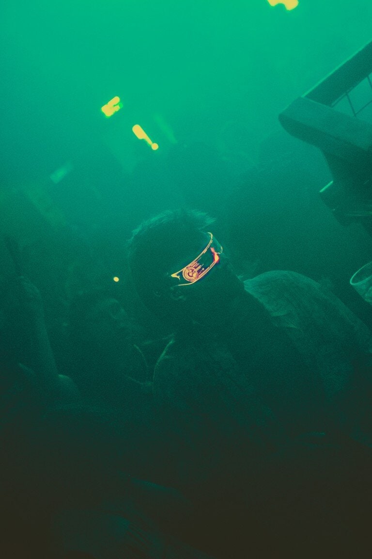 Invisible person wearing futuristic goggles illuminated by colourful LED lights in a dark, vibrant environment.