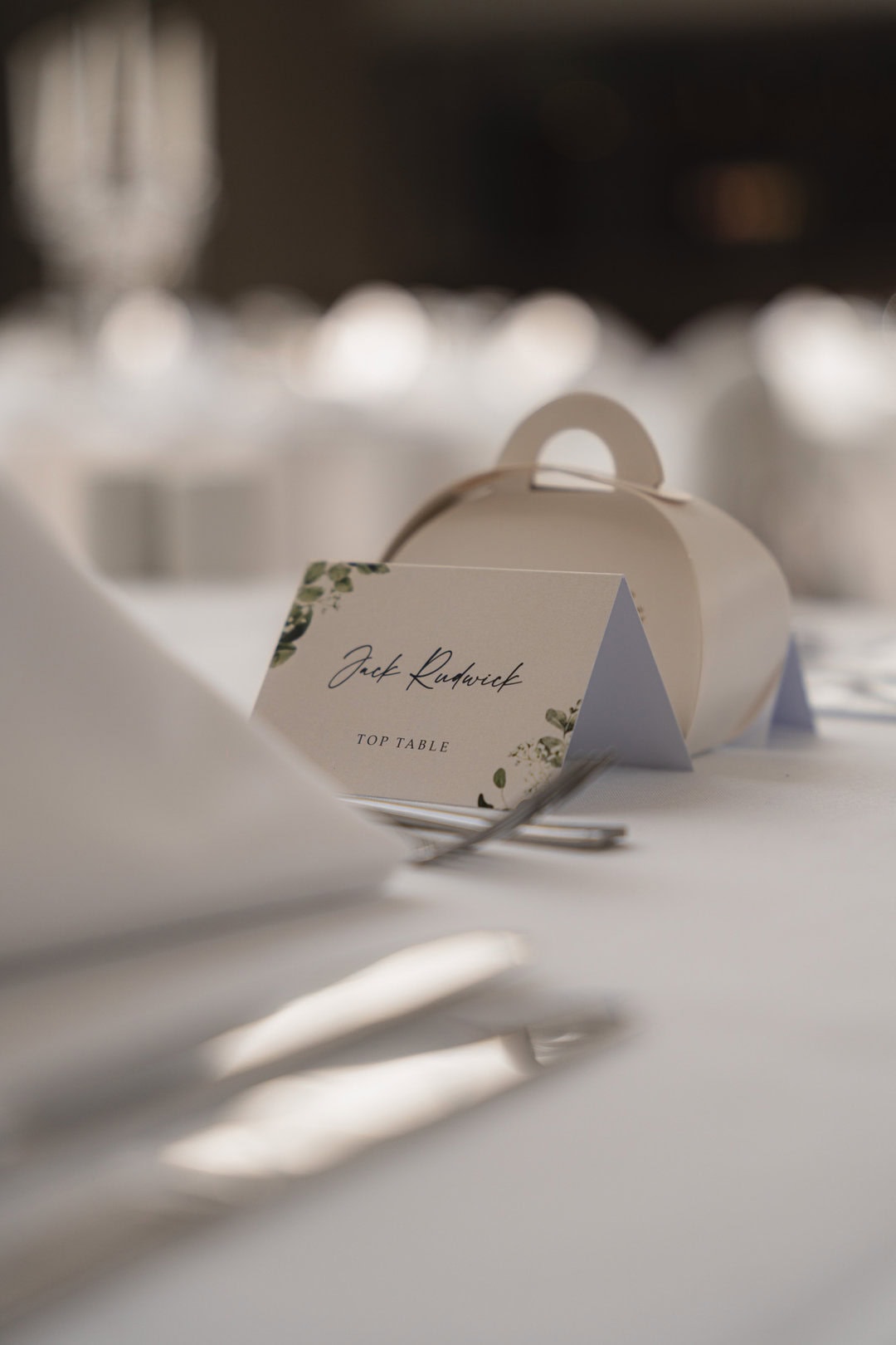 Elegant wedding place card and boxed cutlery set with a soft bokeh background, highlighting attention to detail and sophisticated event décor.