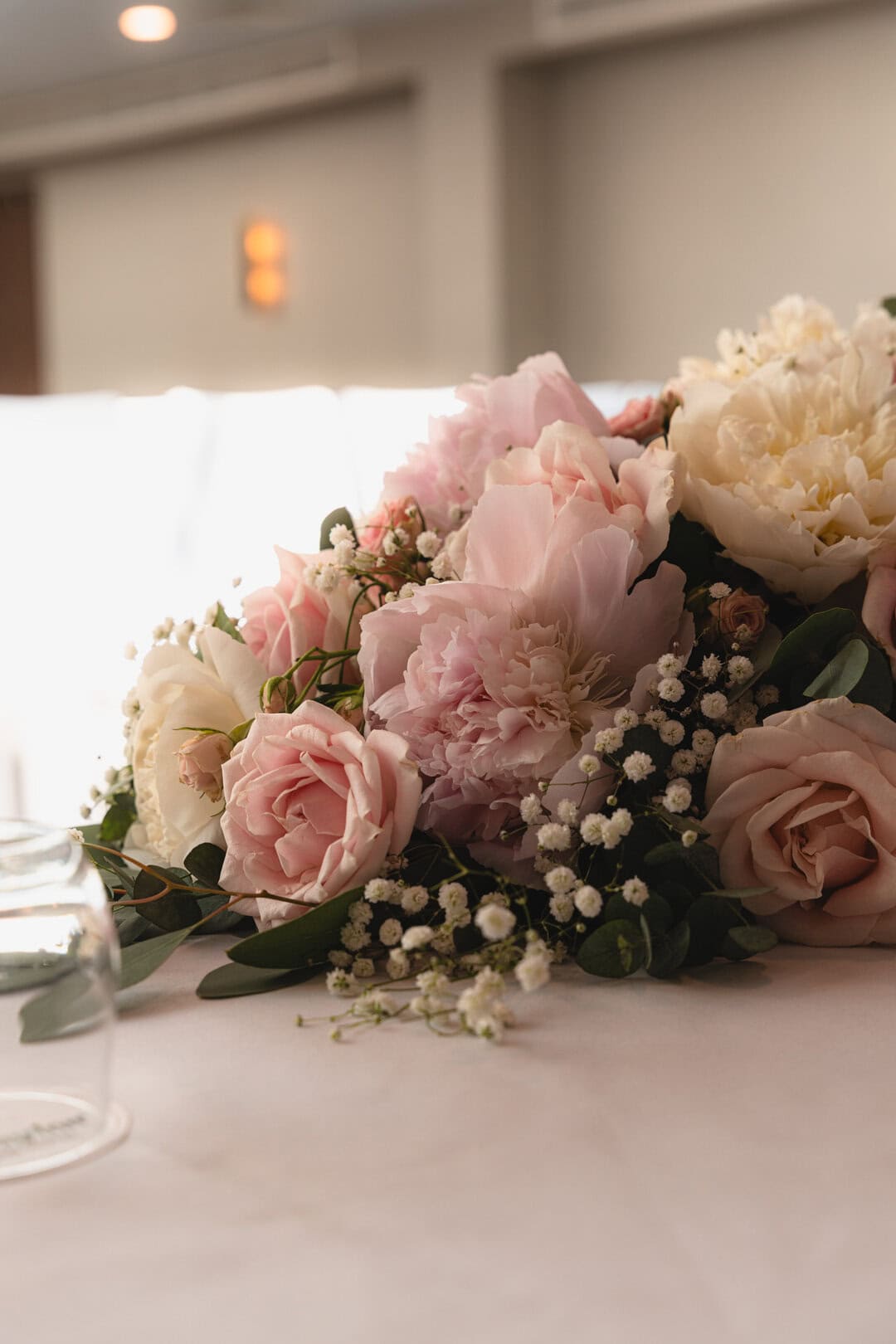 Soft pink and white peony floral arrangement with baby's breath and greenery on a table in an elegant setting.