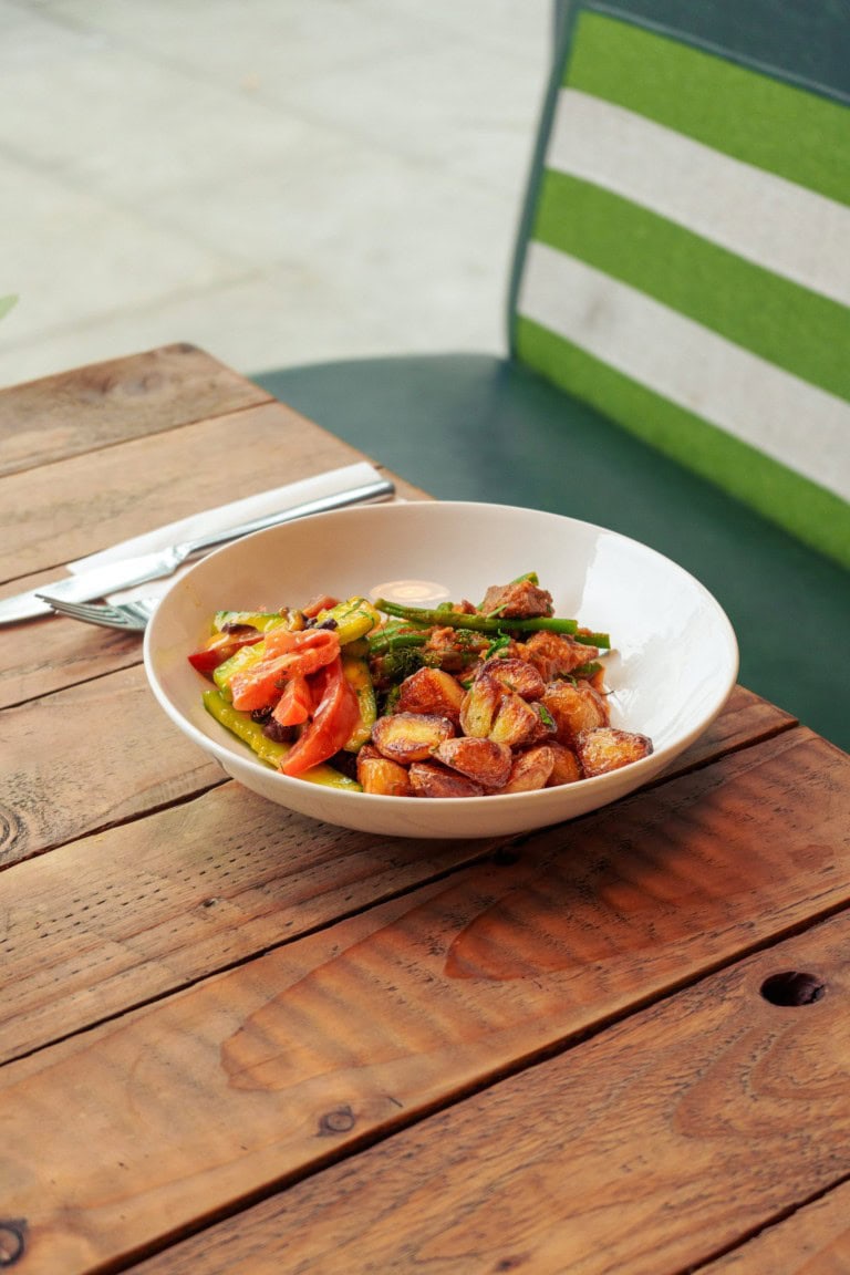A colourful plate featuring freshly cooked vegetables and golden roasted potatoes set on a wooden table.