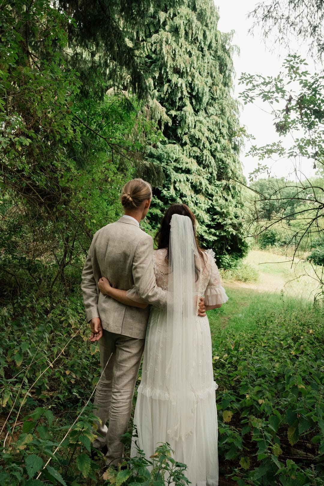 Elegant wedding couple in lush green woodland, capturing natural outdoor wedding photography, romantic bridal couple portrait.