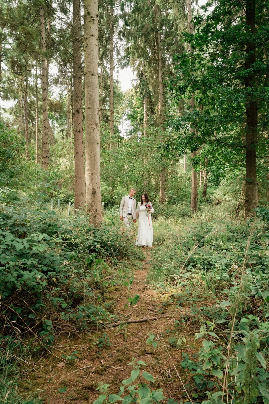 Beautiful forest wedding photography showcasing a couple walking along a lush woodland trail in natural, soft light.