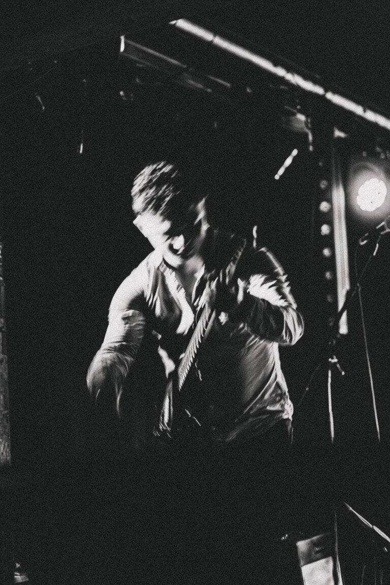 A musician passionately playing an acoustic guitar on stage under dramatic lighting.
