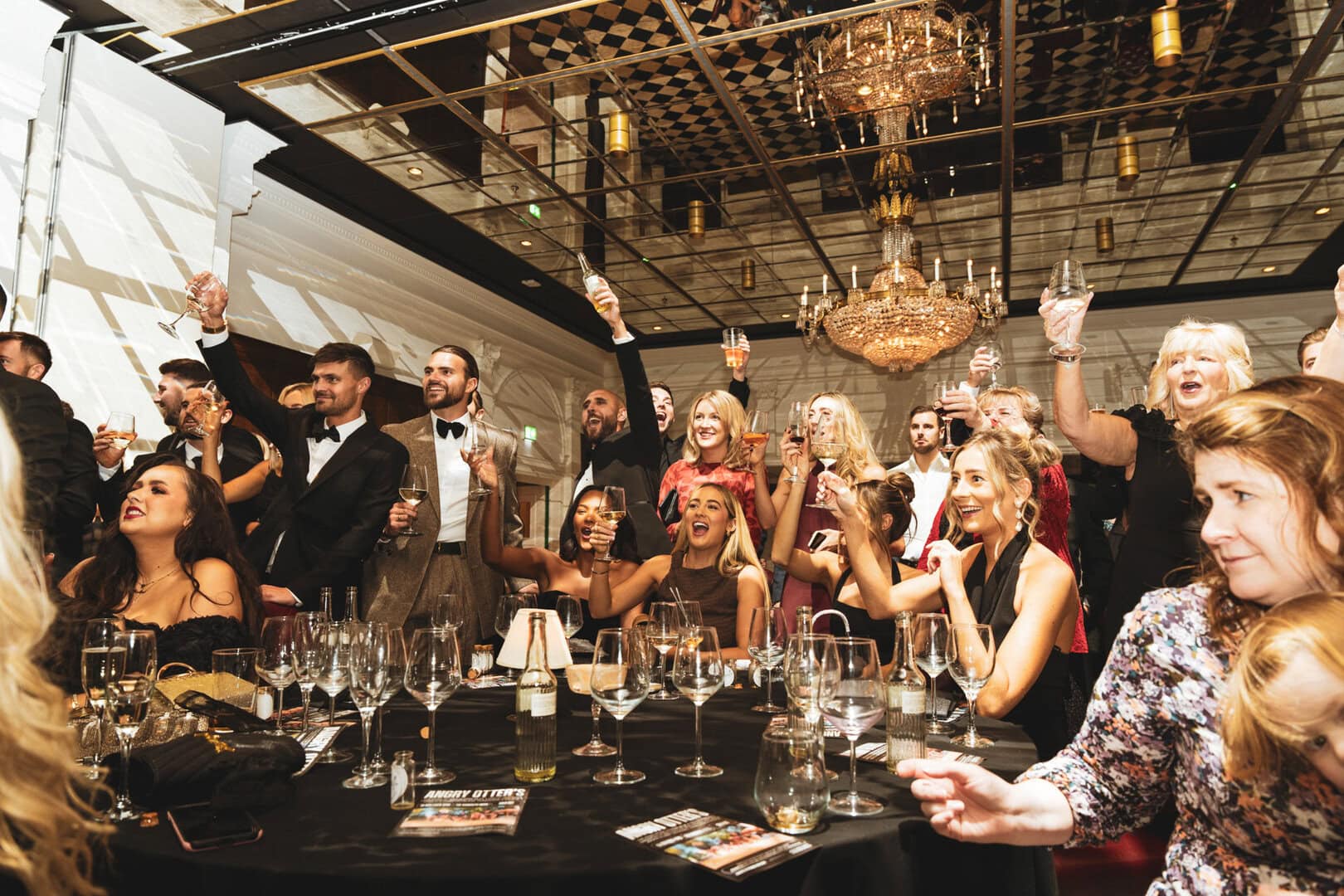 Vibrant group of people celebrating at an elegant banquet, raising glasses in toast, surrounded by sparkling wine and festive atmosphere.